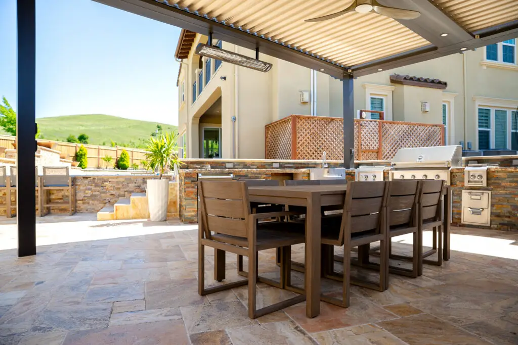 Built-in outdoor kitchen and dining table under a StruXure pergola in Danville, CA, with hillside views