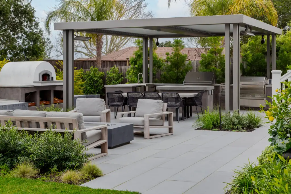 Outdoor kitchen and wood-fired pizza oven near a StruXure pergola in Emerald Hills, CA