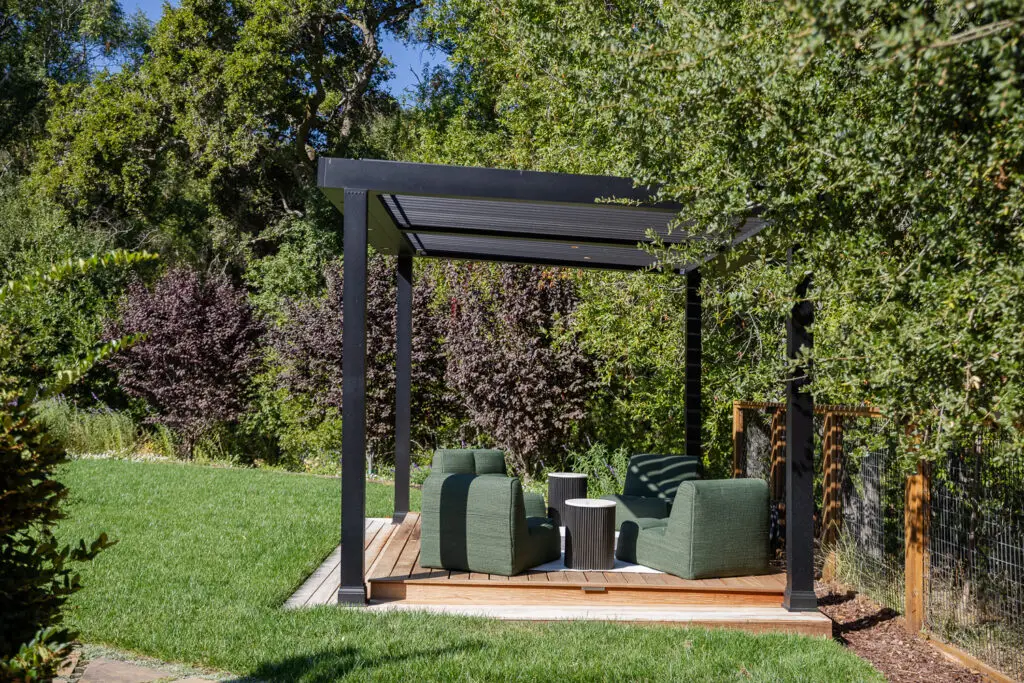 Dense landscaping with dark-leafed shrub behind a StruXure pergola seating area in Saratoga, CA