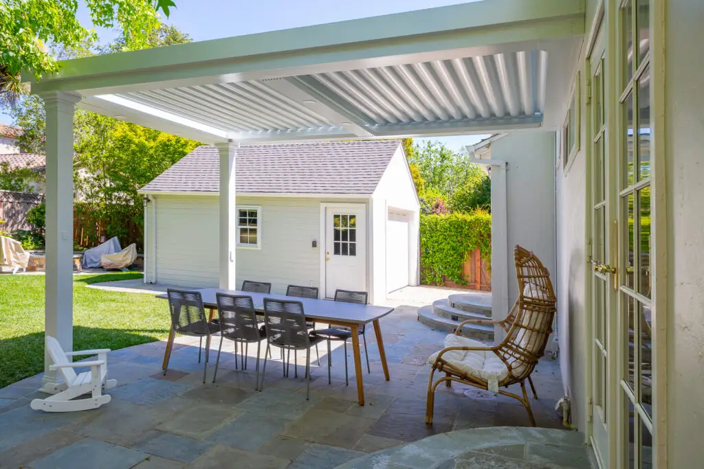 Outdoor dining set and rattan lounge chair under a pergola on a stone patio in Burlingame, CA