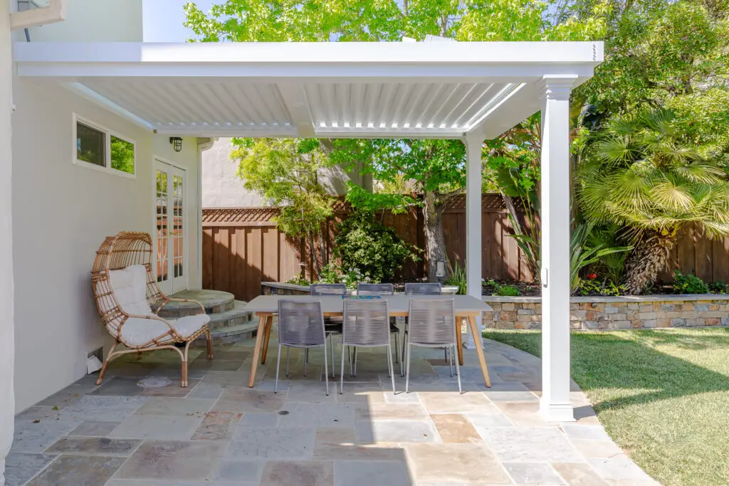 View from underneath a white StruXure pergola roof over a stone patio dining set in Burlingame, CA